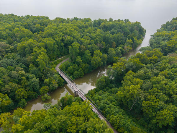 Aerial view of a pedestrian bridge crossing a wooded creek at Charlestown State Park in Southern Indiana, surrounded by dense green forest.