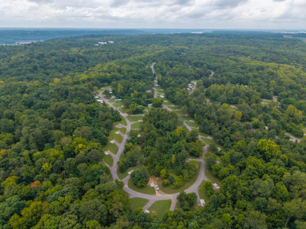 Aerial view of the Charlestown State Park campground surrounded by dense green forest, with winding roads, campsites and RVs visible beneath a cloudy sky.