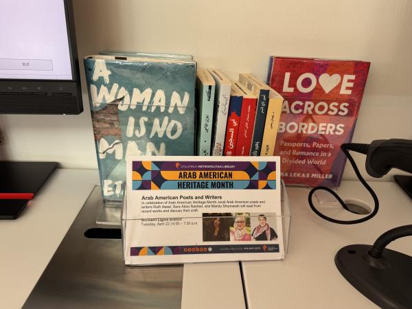 Arab American Heritage Month book display featuring Arabic and English titles, alongside a flyer for a special poetry event at the Columbus Metropolitan Library.