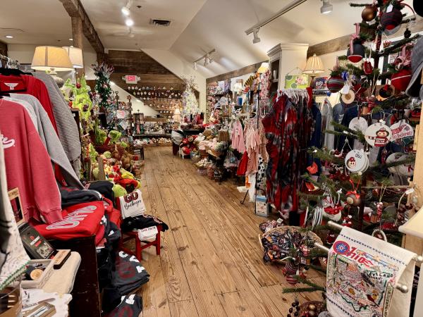 The interior of The Morgan House in Dublin, Ohio, showcasing a festive atmosphere with Christmas decorations and merchandise. The store is filled with various items, including clothing, ornaments, and holiday-themed trinkets. The wooden floors and exposed beams add to the charming ambiance of the shop.