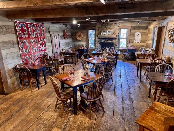 The interior of The Morgan House in Dublin, Ohio, showcasing its rustic dining room. The room features wooden walls and floors, multiple tables with chairs, and a large quilt hanging on the wall. The fireplace adds to the warm and inviting atmosphere of the space.