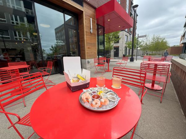 A tray of shrimp and oysters on a red metal table surround by red chairs on the patio of Market Bar at North Market Bridge Park.