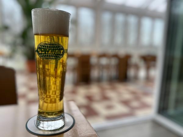 Craft Beer Close-Up (Getaway Brewing): A tall pilsner glass filled with golden beer, topped with a fluffy white foam head. The logo "GETAWAY" is etched on the glass, with a bright, airy conservatory visible in the background.
