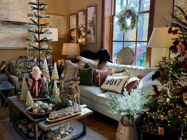 The interior of The Morgan House in Dublin, Ohio, showcasing a festive living room setting. The room features a large window with a wreath, a cozy couch with pillows, a coffee table filled with holiday decorations, and a Christmas tree in the corner. The warm lighting and wooden floors create a welcoming ambiance.
