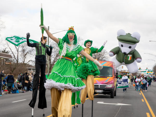 A group of stilt walkers dressed in green performing down the street in the St. Patrick's Day Parade.