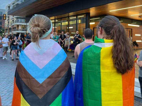 Two young women wearing LGBTQIA+ flags over their shoulders.