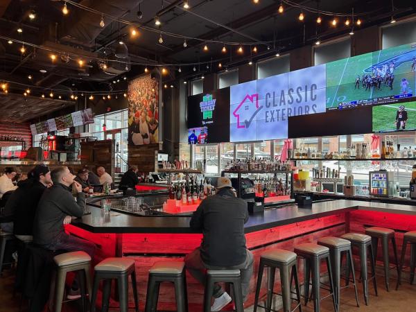 Sports Bar Interior (Urban's Pint House): A modern sports bar with a central bar surrounded by high stools. Large screens display sports games, and string lights add to the lively, welcoming atmosphere.