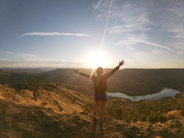 lady on top of mountain with arms raised up while enjoying scenery