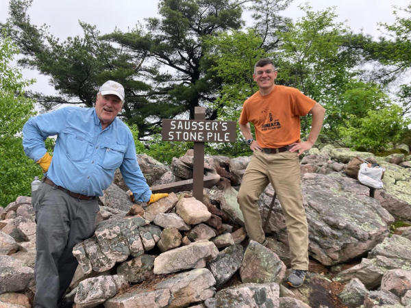 Volunteers Burgess Smith and George Conrad pose in front of the sign for Sausser's Stone Pile along the Standing Stone Trail