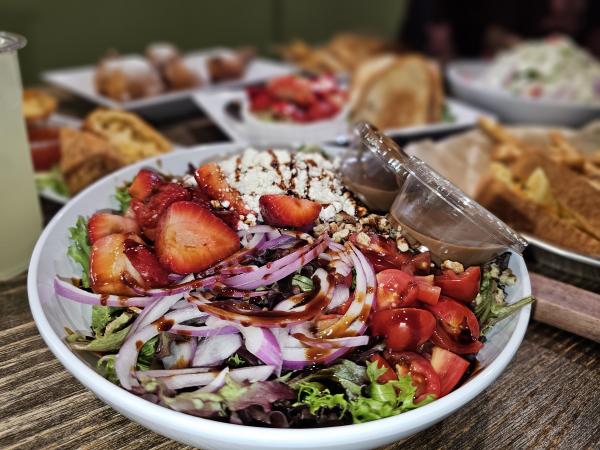 A strawberry salad on a table with plates of food in the background