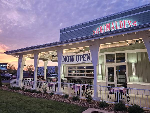 Front of a restaurant under a sunset sky with a "now open" sign