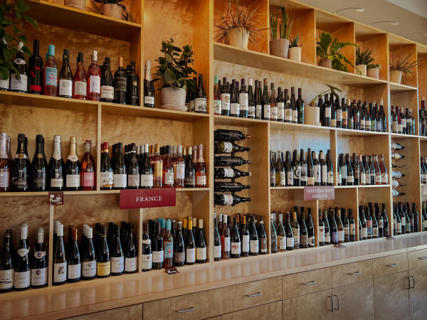 Shelves filled with bottles of wine from France, Washington, Oregon, and other regions, accented with greenery inside Charlie Foster’s in Huntsville.