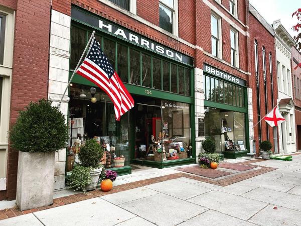 The historic Harrison Brothers Hardware storefront in downtown Huntsville features its iconic green-painted exterior, large display windows, and American and Alabama flags hanging along the sidewalk in front of the longtime local landmark on the courthouse square.