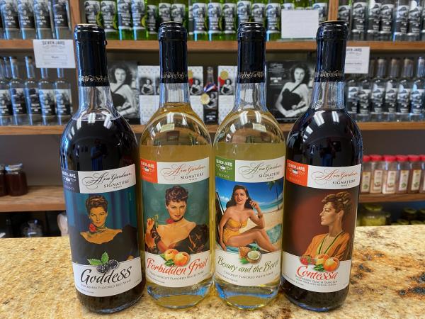 Four bottles of wine from the Ava Gardner Signature Wine Collection, lined up on a bar in front of shelves of alcohol at Seven Jars Distillery.