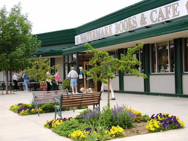 An exterior view of Watermark Books & Cafe in Wichita with two benches in front and blooming yellow and purple flowers