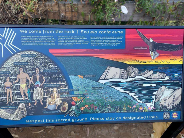 This is an image of an interpretive sign by the indigenous Esselen Tribe in Monterey County, California. The sign is located at Julia Pfeiffer Burns State Park and depicts the Big Sur coastline with a sunset sky, an eagle, and an indigenous family in a traditional home setting