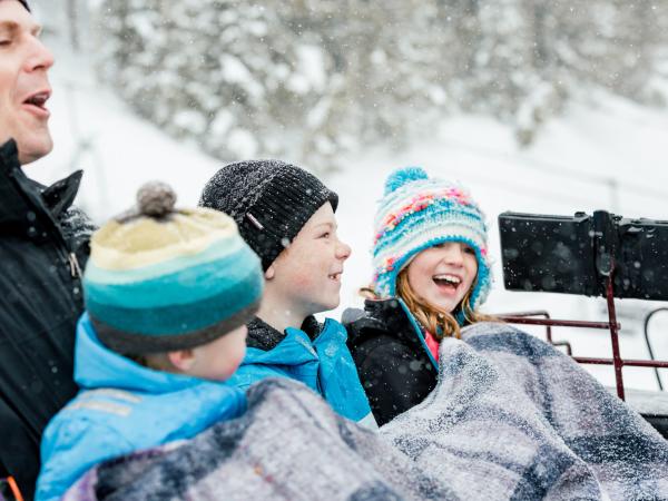 Dad and three children bundled up in a sleigh ride laughing
