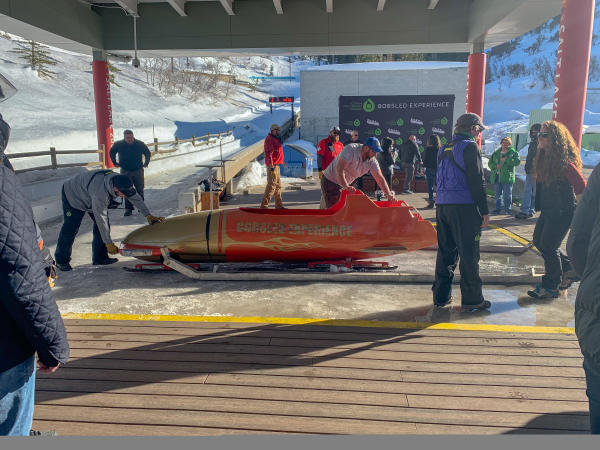 People standing around while two people unload a bobsled off the track