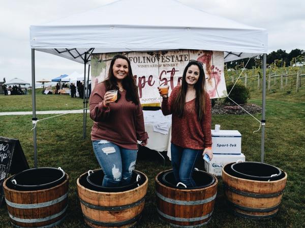 Two women in half barrels holding glasses toast to the grape harvest at Folino Estate Winery.