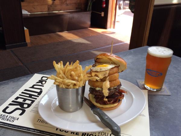 Stacked burger and pail of fries on white plate on top of Druthers menu with beer on the side