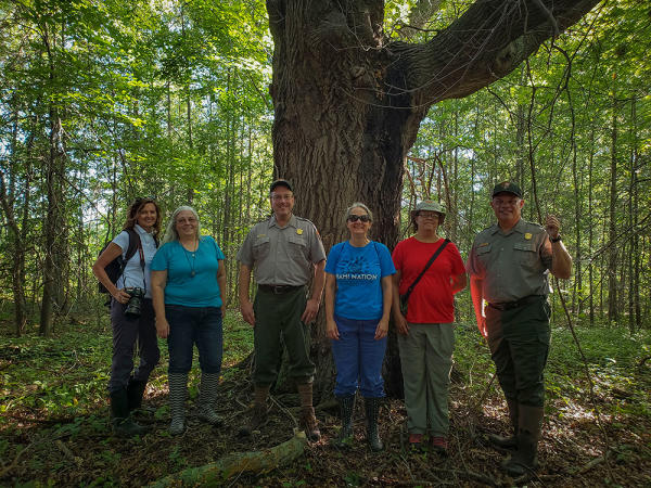 A group of people smile in front of a large tree on the Indiana Dunes Cultural Trail.