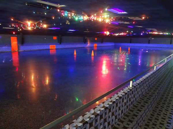 A skating rink floor, dimly lit by colorful lights that ring the floor.