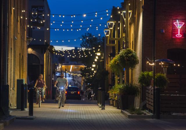 A couple rides bikes in downtown underneath the alley lights