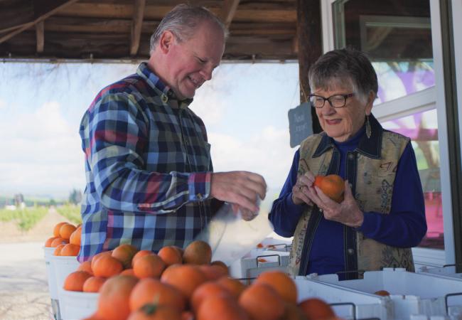 couple smiling while shopping for oranges outside of a food market