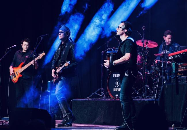 three guitarists and one drummer on stage with theatrical lighting