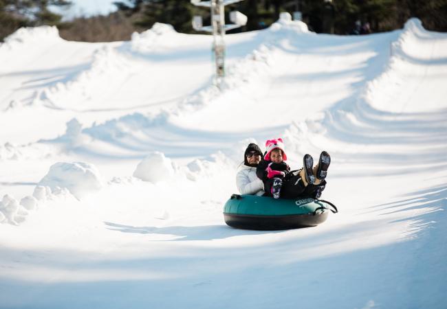 A woman holds a young girl in a snow tube as they glide downhill at Cranmore Mountain
