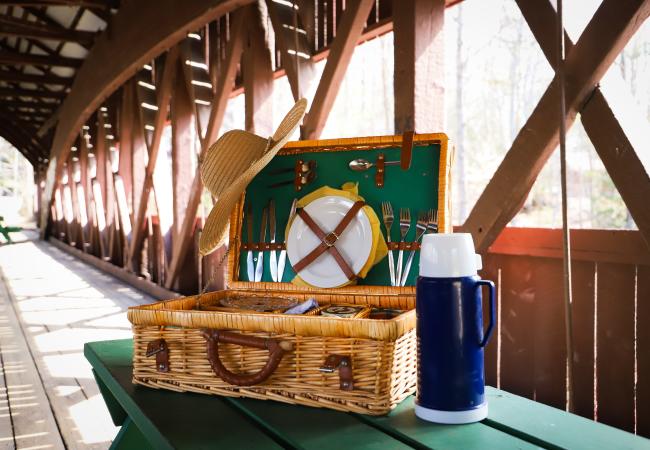 A picnic basket on a green picnic table inside the Swift River Covered Bridge, North Conway