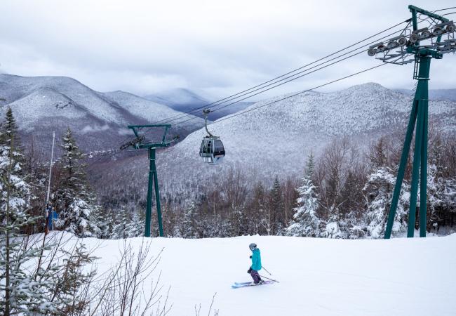 A skier goes downhill underneath a gondola climbing Loon Mountain