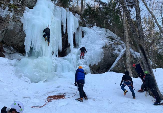 Two people climbing the side of an ice wall as others spot for them at the bottom on an expedition from Ice Climbing with North Country Climbing Center