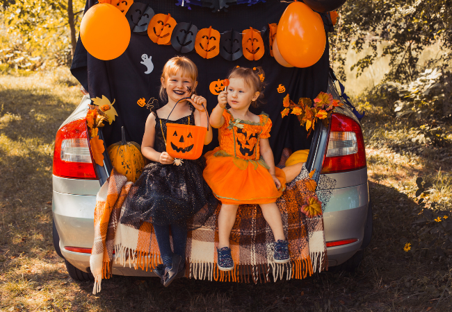 Trunk or Treat Promo Image (Two Girls Wearing Halloween Costumes adn Sitting in Back of Decorated Car)