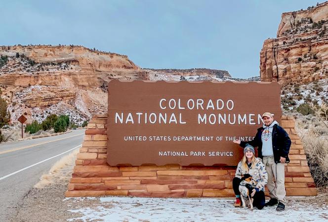 Woman, Man and Dog Standing by Colorado National Monument Sign