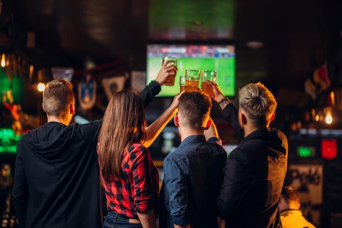 Picture of People Holding Up Beer in Front of TV Screen