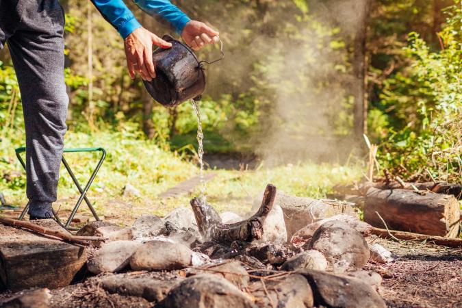 Person pouring water out of a pot onto a fire