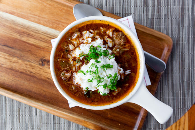 View from above of a white bowl filled with gumbo sitting on a wooden serving plate from Pyre Provisions