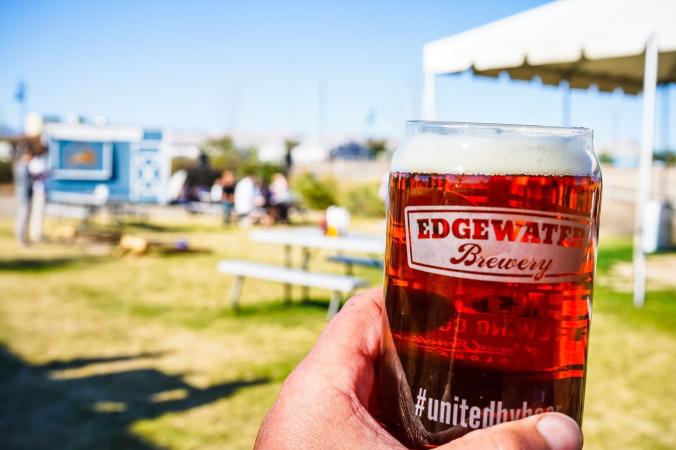 Beer being held with outdoor seating area in background at Edgewater Brewery