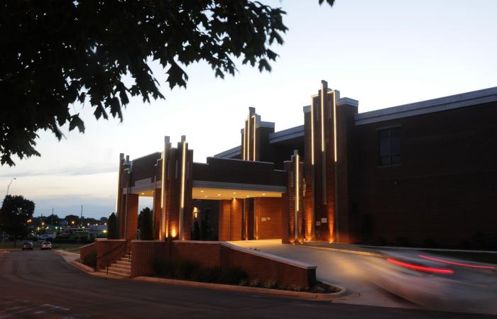 Exterior of Campus No. 805 in Huntsville at dusk, featuring the historic brick building illuminated with warm lights and a car passing beneath the covered entrance.