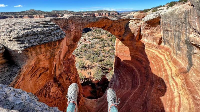 Hiker sits on top of the Cedar Tree Arch Overlook in Rattlesnake Arches