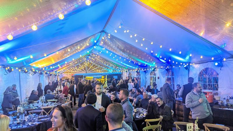 A large event tent with globe lights. People mingle around and tables are set for the tasting dinner.