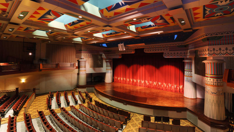 Several rows of theater seats facing wooden stage with red curtain
