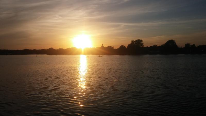 Golden warm sunset shines on Canandaigua Lake with two kayaks crossing in front of Kershaw Park's swimming area.