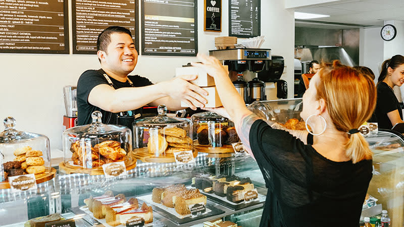 A barista at Bonjour Cafe is giving a customer boxes of pastries.