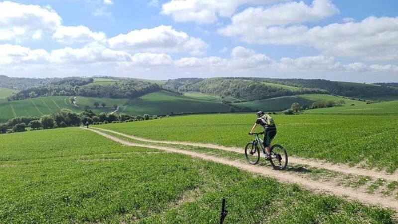 A person riding a mountain bike on the south downs way with rolling hills in the background