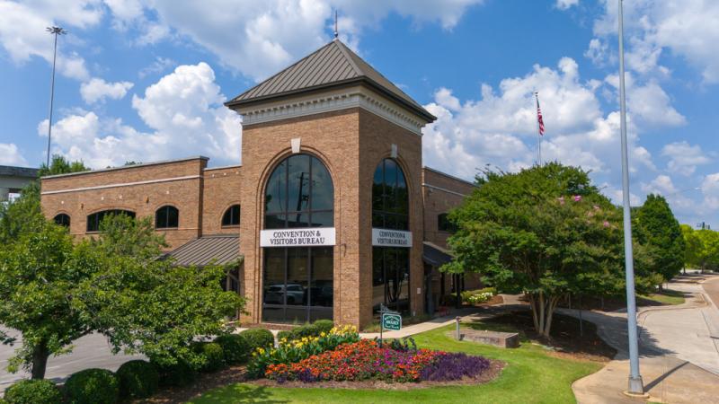 exterior view of the Huntsville/Madison County Convention & Visitors Bureau visitor Center in summer with flowers blooming and blue skies with puffy white clouds in the background