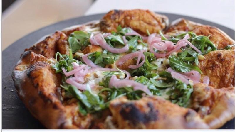 A pizza topped with greens and red onions with a bubbly crust from Annie's Beach Cafe at Frind Winery
