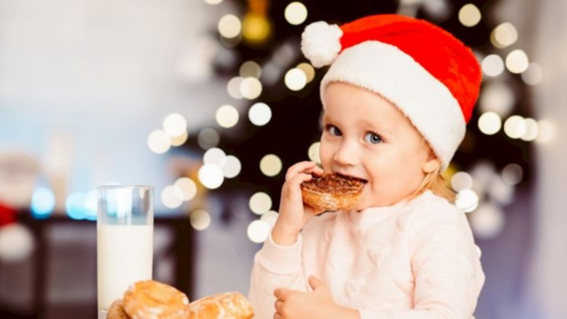 Child eating a donut with a Santa hat on