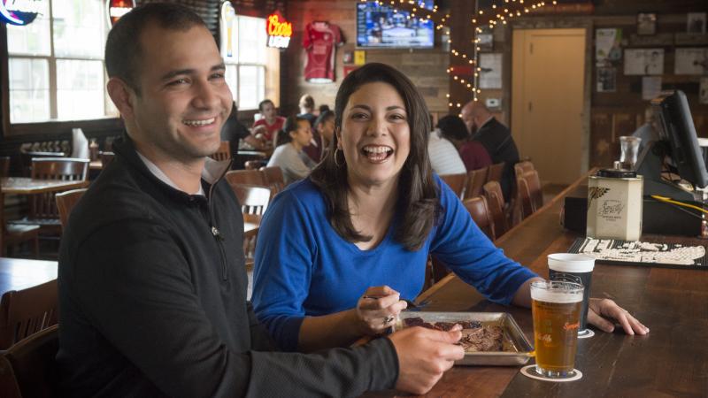 Man and woman eating at restaurant with meeting group behind them